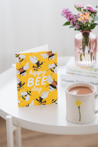 happy bee day plantable birthday card on white coffee table with vase of wildflowers and a cup of tea